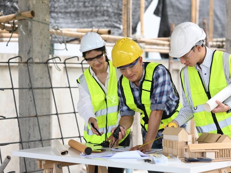 Construction project management team reviewing plans and building models at an active construction site.