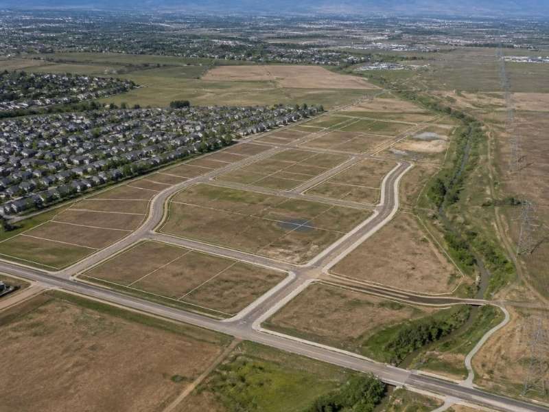 Aerial view of a planned land development site near Denver with roads, residential neighborhoods, open land, and the Rocky Mountains.
